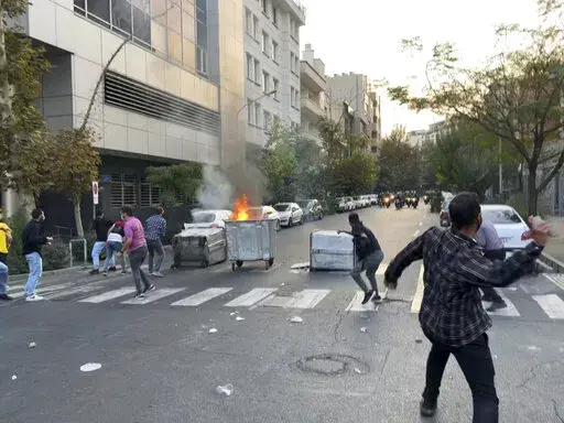In this Tuesday, Sept. 20, 2022, photo taken by an individual not employed by the Associated Press and obtained by the AP outside Iran, protesters throw stones at anti-riot police during a protest over the death of a young woman who had been detained for violating the country's conservative dress code, in downtown Tehran, Iran. Iran faced international criticism on Tuesday over the death of a woman held by its morality police, which ignited three days of protests, including clashes with security