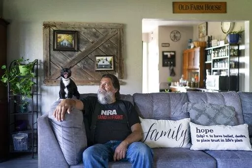 John Kraft sits next to his yawning cat, Tux, at his hilltop farmhouse in Clear Lake, Wis., Wednesday, Sept. 28, 2022. Kraft loves this place. He loves the quiet and the space but looks beyond his rural community and sees a country that many Americans wouldn't recognize. It's a dark place, dangerous, where democracy is under attack by a tyrannical government, few officials can be trusted and clans of neighbors might someday have to band together to protect one another. (AP Photo/David Goldman)