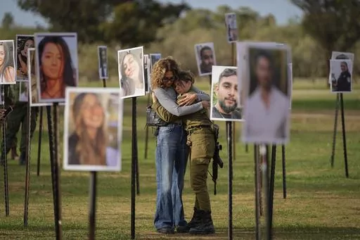 Israelis embrace next to photos of people killed and taken captive by Hamas militants during their violent rampage through the Nova music festival in southern Israel, which are displayed at the site of the event, as Israeli DJs spun music, to commemorate the October 7, massacre, near kibbutz Re'im, Tuesday, Nov. 28, 2023. Nearly two months after Hamas infiltrated Israel, killing some 1,200 people and taking about 240 hostage, dozens are still unaccounted for, their families left living in limbo.