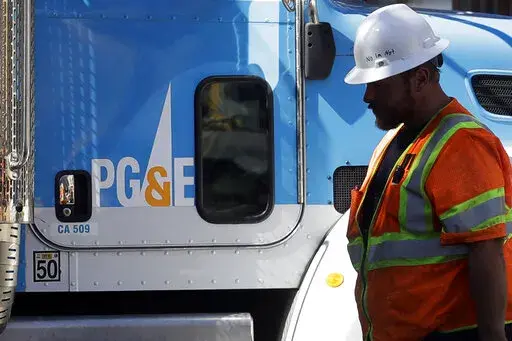 In this Aug. 15, 2019, file photo, a Pacific Gas & Electric worker walks in front of a truck in San Francisco. Pacific Gas & Electric has agreed to pay more than $55 million to avoid criminal prosecution for two major wildfires started by its aging equipment in 2019 and 2021, prosecutors announced. (AP Photo/Jeff Chiu, File)