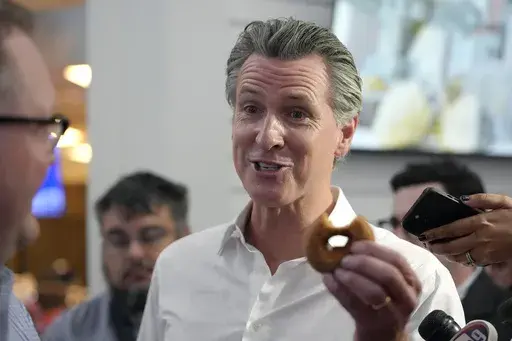 California Gov. Gavin Newsom holds a donut while greeting people, Monday, July 8, 2024, near the Common Man Roadside Market and Deli, in Hooksett, N.H. (AP Photo/Steven Senne)