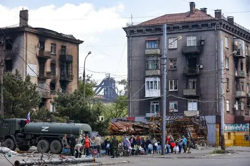 Local civilians gather to receive pure water distributed by Russian Emergency Situations Ministry in Mariupol, in territory under the government of the Donetsk People's Republic, eastern Ukraine, on May 27, 2022, with the Illich Iron & Steel Works Metallurgical Plant is in the background. According to Russian state TV, the future of the Ukrainian regions occupied by Moscow's forces is all but decided: Referendums on becoming part of Russia will soon take place there, and the joyful residents who