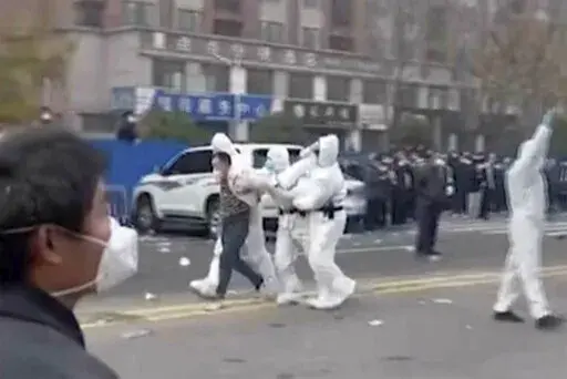 In this photo provided Nov 23, 2022, security personnel in protective clothing were seen taking away a person during protest at the factory compound operated by Foxconn Technology Group who runs the world's biggest Apple iPhone factory in Zhengzhou in central China's Henan province. Employees at the world's biggest Apple iPhone factory were beaten and detained in protests over pay amid anti-virus controls, according to witnesses and videos on social media Wednesday, as tensions mount over Chines