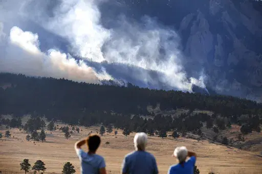 From left, Laura Tyson, Tod Smith and Rebecca Caldwell, residents of Eldorado Springs, watch as the NCAR fire burns in the foothills south of the National Center for Atmospheric Research, Saturday, March 26, 2022, in Boulder, Colo. The NCAR fire prompted evacuations in south Boulder and pre-evacuation warning for Eldorado Springs. According to a study published in Science Advances on Friday, April 1, 2022, a one-two punch of nasty wildfires followed by heavy downpours, triggering flooding and mu