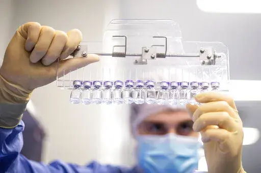 In this photo provided by Pfizer, a technician inspects filled vials of the Pfizer-BioNTech COVID-19 vaccine at the company's facility in Puurs, Belgium in March 2021. COVID-19 vaccines are saving an untold number of lives but they can't stop the chaos when a hugely contagious new mutant bursts on the scene, leading people to wonder: Will we need boosters every few months? A new vaccine recipe? A new type of shot altogether? (Pfizer via AP)