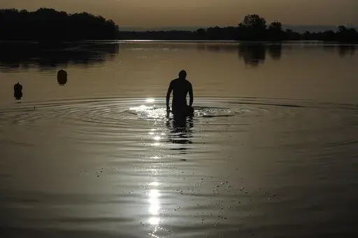 A man walks in the water as the sun rises above the Miribel lake, outside Lyon, central France, Saturday, June 18, 2022. A heat wave that's already lasted more than a week keeps on baking the US, Asia, Europe and even the Arctic. (AP Photo/Laurent Cipriani, File)
