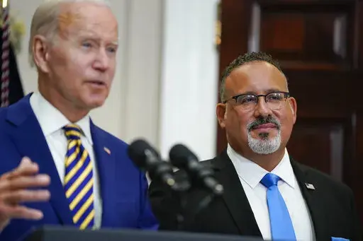 Education Secretary Miguel Cardona listens as President Joe Biden speaks about student loan debt forgiveness in the Roosevelt Room of the White House, Wednesday, Aug. 24, 2022, in Washington. (AP Photo/Evan Vucci)