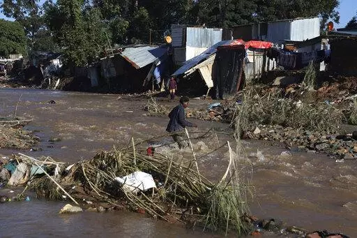 A man crosses a river at an informal settlement during flooding in Durban, South Africa, Thursday, April 14, 2022. Heavy rains and flooding have killed at least 341 people in South Africa's eastern KwaZulu-Natal province, including the city of Durban, and more rainstorms are forecast in the coming days. (AP Photo/Str)