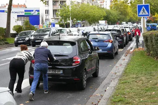 People push their car in a line of vehicles waiting to reach a station, Friday, Oct. 14, 2022 in Nanterre, outside Paris. Strikes in the French refineries of TotalEnergies group were still going on Friday, heavily disrupting fuel supplies as hard-left CGT union rejected a deal over pay rise that has been found between the energy giant and two other more moderate unions. (AP Photo/Michel Euler)