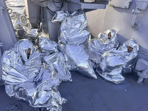 In this photo provided by the Greek Coast Guard, some of the nine men who survived a shipwreck and were found on an uninhabited islet are covered with a thermal blankets as they sit aboard a Greek Coast guard vessel, in the Aegean Sea, Greece, on Tuesday, Nov. 1, 2022. A major search and rescue operation was underway Tuesday for dozens of people missing after the boat they were on capsized and sank in stormy weather overnight off the coast of an island near the Greek capital. The coast guard sai
