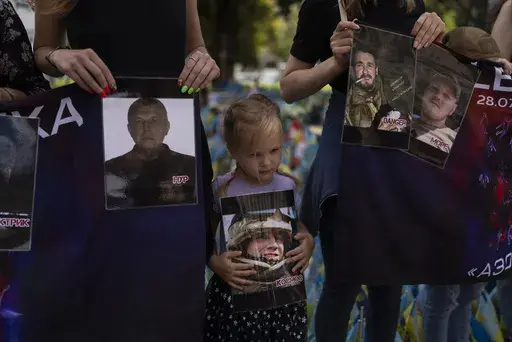 A girl holds a photo of a Ukrainian POW killed in the 2022 explosions at the Russian-controlled prison barracks in Olenivka, eastern Ukraine, during a memorial in Kyiv on July 29, 2023. An AP investigation interviewed survivors, family and investigators and obtained an internal U.N. analysis. All pointed to Russia as the culprit. (AP Photo/Jae C. Hong, File)