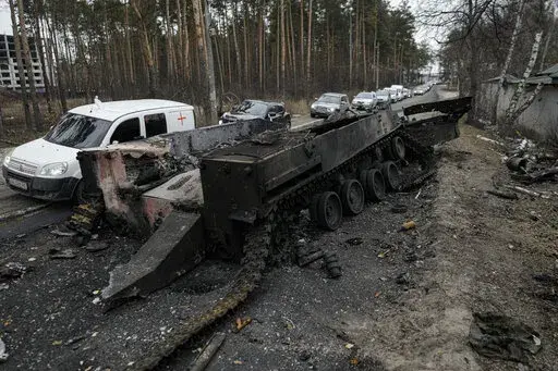 Cars drive past a destroyed Russian tank as a convoy of vehicles evacuating civilians leaves Irpin, on the outskirts of Kyiv, Ukraine, March 9, 2022. Thousands of patients in Ukraine are receiving lifesaving medicines to treat HIV and opioid addiction through a U.S.-funded group still operating despite the Russian invasion. Supplies are running short and making deliveries is a complicated calculus with unpredictable risks. (AP Photo/Vadim Ghirda, File)