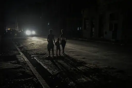 Residents are illuminated by the headlights of a car during a blackout after a major power plant failed in Havana, Cuba, Oct. 18, 2024. (AP Photo/Ramon Espinosa, File)