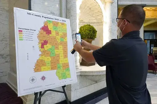 A visitor to the Mississippi Capitol in Jackson, uses his cell phone to photograph a graphic of the state that depicts census growth or loss in each county over a 10-year period in Jackson, Miss., Thursday, Aug. 26, 2021. (AP Photo/Rogelio V. Solis)