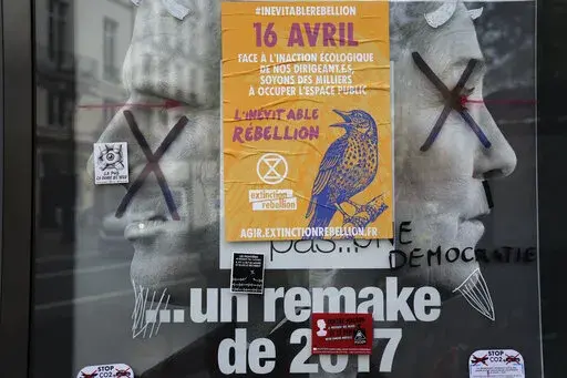 A torn front page ad shows incubent President Emmanuel Macron and challenger Marine Le Pen as the environmental group Extinction Rebellion takes part in a three-day demonstration against what they call France's inaction on climate issues, in the district of Porte de Saint Denis in the center of Paris, France, Monday, April 18, 2022. French President Emmanuel Macron is in pole position to win reelection Sunday, April 24, 2022 in France's presidential runoff. Yet his lead over far-right rival Mari