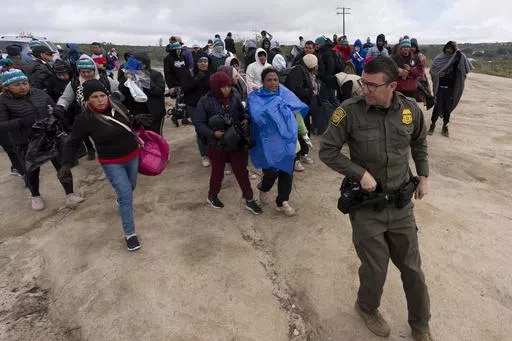 People seeking asylum, including a group from Peru, walk behind a Border Patrol agent towards a van to be processed after crossing the border with Mexico nearby, on April 25, 2024, in Boulevard, Calif. President Joe Biden has ordered a halt to asylum processing at the U.S. border with Mexico when arrests for illegal entry top 2,500 a day, which was triggered immediately. (AP Photo/Gregory Bull, File)
