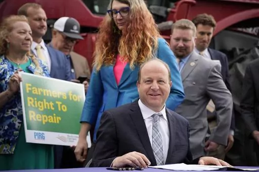 Colorado Gov. Jared Polis, front, waits to sign legislation that forces manufacturers to provide the necessary manuals, tools, parts and even software to farmers so they can fix their own machines, Tuesday, April 25, 2023, during a ceremony outside the State Capitol in Denver. Colorado is the first state to put the right-to-repair law into effect while at least 10 other states are considering similar measures. Colorado State Rep. Brianne Titone, center, and Rep. Ron Weinberg, back, head in to wi
