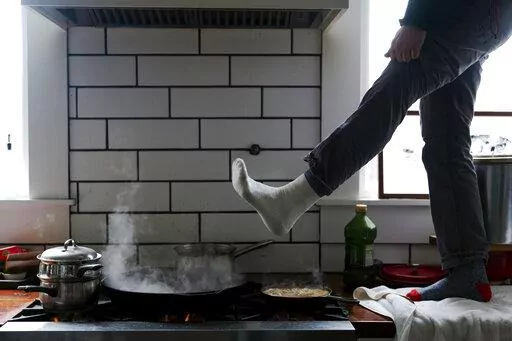 Jorge Sanhueza-Lyon stands on his kitchen counter to warm his feet over his gas stove during a snow storm on Feb. 16, 2021, in Austin, Texas. Following comments made by a member of the Consumer Product Safety Commission on Jan. 9, 2023, misleading claims that the Biden administration is planning on banning gas stoves have spread widely across social media platforms. (AP Photo/Ashley Landis, File)