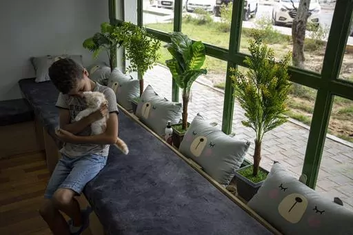 A Palestinian child enjoys the company of a cat on the opening day of Meow Cafe, Gaza City, Thursday, Aug 17, 2023. Amidst the challenges of life in the Gaza Strip, constrained by a 17-year blockade and ongoing conflicts, this first-ever cat cafe offers a unique space for relaxation and positive human-animal interaction. (AP Photo/Fatima Shbair)