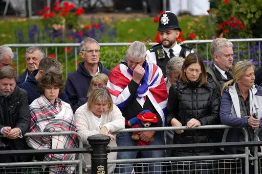 Members of the public, one of them holding a Paddington Bear toy, outside Buckingham Palace wait to watch Queen Elizabeth II funeral procession, in central London on Monday, Sept. 19, 2022. (AP Photo/Christophe Ena, Pool)
