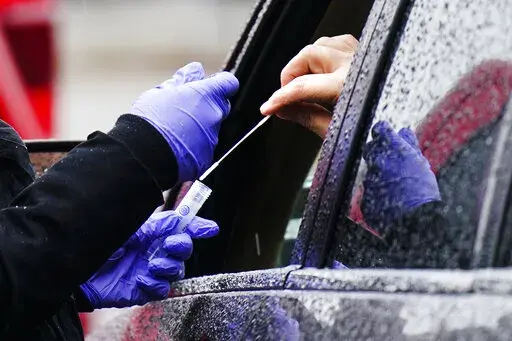 A driver places a swab into a vial at a free drive-thru COVID-19 testing site in the parking lot of the Mercy Fitzgerald Hospital in Darby, Pa., Thursday, Jan. 20, 2022. A requirement to get vaccinated against COVID-19 kicks in Thursday, Jan. 27,  for millions of health care workers in about half the states. (AP Photo/Matt Rourke, File)
