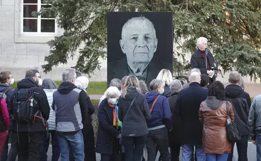 Participants of a memorial service for Buchenwald survivor Boris Romantschenko stand in front of his photo in Weimar, Germany Tuesday, March 22, 2022. Germany’s parliament has paid tribute to Boris Romanchenko, who survived several Nazi concentration camps during World War II but was killed last week during an attack in the Ukrainian city of Kharkiv. He was 96. (Bodo Schackow/dpa via AP)