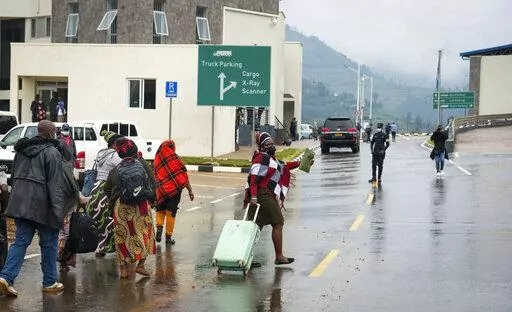A Ugandan woman holds her arm up to celebrate as she and her group cross the border to attend the funeral of one of their mothers who had died in Rwanda, at the Uganda-Rwanda border crossing in Katuna, Uganda Monday, Jan. 31, 2022. Rwandan authorities on Monday opened the Uganda border to truckers after nearly three years of a tense standoff, but other non-essential travelers were held back by immigration officials. (AP Photo/Hajarah Nalwadda)