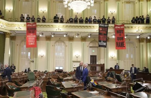 Assembly members Heath Flora, R-Modesto, left, and Josh Lowenthal, D-Long Beach, right, leave the Assembly chambers as protesters call for a cease-fire in Gaza disrupt the first day of the California legislative session in Sacramento, Calif., Wednesday, Jan. 3, 2024. The Assembly session was just getting started when protesters wearing matching black t-shirts stood up in the gallery and started singing "Cease-fire now" and "Let Gaza Live." The Assembly adjourned the session.(AP Photo/Rich Pedron