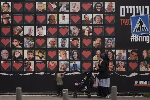 A woman and her children walk past a wall with photographs of hostages who were kidnapped during the Oct. 7, 2023, Hamas cross-border attack in Israel, Feb. 26, 2024, in Jerusalem. On Monday, June 24, Israelis who were taken hostage or lost loved ones during the attack filed suit against the United Nations agency that aids Palestinians, claiming it has helped finance the militants by paying agency staffers in U.S. dollars and thereby funneling them to money-changers in Gaza who allegedly give a 