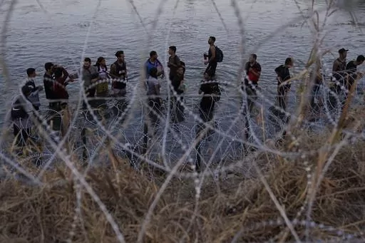 Migrants wait to climb over concertina wire after they crossed the Rio Grande and entered the U.S. from Mexico, Saturday, Sept. 23, 2023, in Eagle Pass, Texas. Abbott is expected to sign into law sweeping new powers that allow police to arrest migrants who cross the border illegally and gives local judges authority to order them to leave the country. (AP Photo/Eric Gay, File)