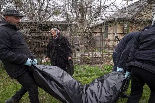 Vlad Minchenko, left, carries a plastic bag with the dead body of Stanislav Berestnev who died during the Russian occupation and was buried in the graveyard in Bucha, Ukraine, Tuesday, April 19, 2022. Minchenko wakes every day with trembling hands. For hours, until it eases, he can't message on his phone or even consider his previous work of making art or tattoos. But he can continue to retrieve bodies, scores of bodies, around the Ukrainian town of Bucha as part of a task that continues more th