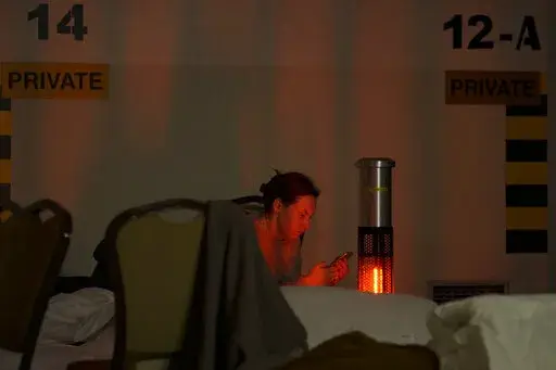 A woman looks at her mobile phone in a hotel underground parking turned into a bomb shelter during an air raid alert in Kyiv, Ukraine, Sunday, Feb. 27, 2022. Terrified men, women and children sought safety inside and underground, and the government maintained a 39-hour curfew to keep people off the streets as more than 150,000 Ukrainians fled to neighboring countries and the United Nations warned the number could grow to 4 million if fighting escalates.(AP Photo/Vadim Ghirda)