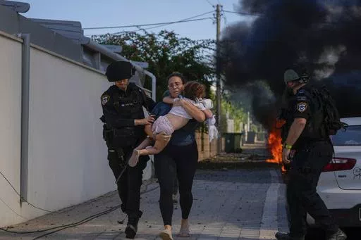 Israeli police officers evacuate a woman and a child from a site hit by a rocket fired from the Gaza Strip, in Ashkelon, southern Israel, Saturday, Oct. 7, 2023. Thousands of Hamas-led militants storm across the border into Israel, killing 1,200 people, mostly civilians, and taking roughly 250 captive, according to Israeli authorities. (AP Photo/Tsafrir Abayov, File)