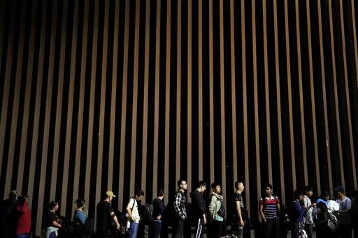 People line up against a border wall as they wait to apply for asylum after crossing the border from Mexico, July 11, 2023, near Yuma, Ariz. An appeals court Thursday, Aug. 3, allowed a rule restricting asylum at the southern border to stay in place. The decision is a major win for the Biden administration, which had argued that the rule was integral to its efforts to maintain order along the U.S.-Mexico border. (AP Photo/Gregory Bull, File)