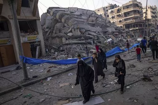 Palestinians walk by the rubble of a building after it was struck by an Israeli airstrike, in Gaza City, Sunday, Oct. 8, 2023. The militant Hamas rulers of the Gaza Strip carried out an unprecedented, multi-front attack on Israel at daybreak Saturday, firing thousands of rockets as dozens of Hamas fighters infiltrated the heavily fortified border in several locations by air, land, and sea, killing hundreds and taking captives. Palestinian health officials reported scores of deaths from Israeli a