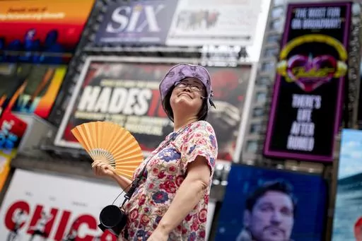 A tour guide fans herself while working in Times Square as temperatures rise, July 27, 2023, in New York. Nearly 60% of the U.S. population, are under a heat advisory or flood warning or watch as the high temperatures spread and new areas are told to expect severe storms. (AP Photo/John Minchillo, File)