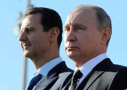Russian President Vladimir Putin, right, and Syrian President Bashar Assad watch troops marching at the Hemeimeem air base in Syria, on Dec. 11, 2017. (Mikhail Klimentyev, Sputnik, Kremlin Pool Photo via AP, File)