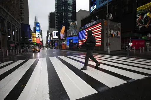 A man crosses the street in a nearly empty Times Square, which is usually very crowded on a weekday morning in New York on March 23, 2020. (AP Photo/Mark Lennihan, File)