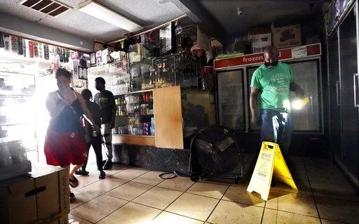 Keith, right, uses a flashlight to help others shop in the dark at a convenience store after the effects the effects of Hurricane Ida knocked out power in the area, Monday, Aug. 30, 2021, in New Orleans, La. (AP Photo/Eric Gay)