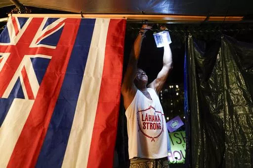 Naldo Valentine, who lost his home to the Lahaina wildfire, puts up a light as darkness falls at a housing protest on Kaanapali Beach Wednesday, Dec. 6, 2023, in Lahaina, Hawaii. A group of survivors were camping on the resort beach to protest and raise awareness for better long-term housing options for those displaced. (AP Photo/Lindsey Wasson, File)