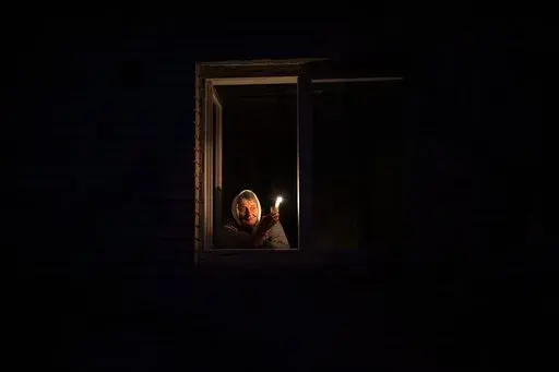 Catherine, 70, looks out the window while holding a candle for light inside her house during a power outage, in Borodyanka, Kyiv region, Ukraine, Thursday, Oct. 20, 2022. Airstrikes cut power and water supplies to hundreds of thousands of Ukrainians on Tuesday, part of what the country's president called an expanding Russian campaign to drive the nation into the cold and dark and make peace talks impossible. (AP Photo/Emilio Morenatti)