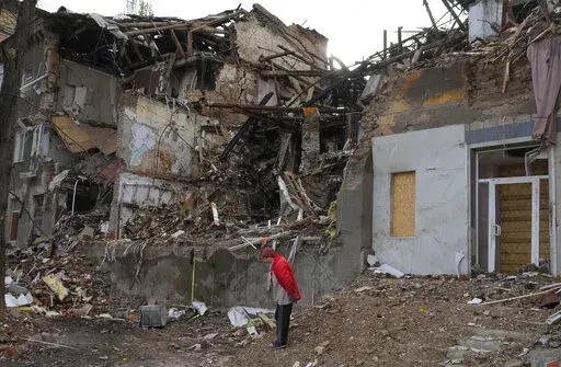 Local resident Nina, 72, stands near her house, ruined by the Russian shelling a month ago in central Slavyansk, Donetsk region, Ukraine, Saturday, Oct. 29, 2022. She keeps living in this house and collects wooden debris to make an outdoor fire for cooking. (AP Photo/Efrem Lukatsky)