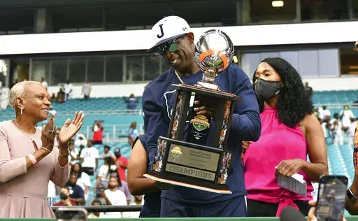 Jackson State head football coach Deion Sanders, center, holds the Orange Blossom Classic trophy after winning an NCAA college football game over Florida A&M, Sunday, Sept. 5, 2021, in Miami Gardens, Fla. (AP Photo/Jim Rassol)