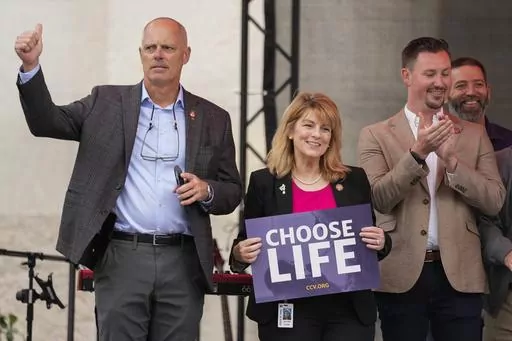 Ohio State Rep. Jennifer Gross, R-West Chester, holding a "Choose Life" sign, center, joined by Ohio State Rep. Adam Bird, R-New Richmond, left, and Ohio State Rep. Thomas Hall, R-Madison Township, right, stand together on stage during the Ohio March for Life rally at the Ohio State House in Columbus, Ohio, Oct. 6, 2023. The statewide battles over abortion rights that have erupted since the U.S. Supreme Court overturned a constitutional right to the procedure have exposed another fault line: com