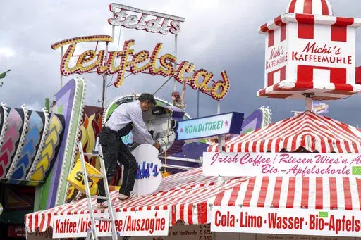 A man mounts a light advertisement on a booth on the Oktoberfest grounds in Munich, Germany, Thursday, Sept. 15, 2022. The Oktoberfest is on tap again in Germany after a two-year pandemic interruption. The beer will be just as cold and the pork knuckle just as juicy. But brewers and visitors are under pressure from inflation in ways they could hardly imagine in 2019. (Peter Kneffel/dpa via AP)