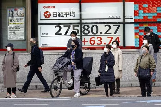 People wait for a traffic light to change in front of an electronic stock board showing Japan's Nikkei 225 index at a securities firm Thursday, March 2, 2023, in Tokyo. Asian stock markets were mixed Thursday after signs of enduring upward pressure on American prices added to expectations of higher interest rates for longer. (AP Photo/Eugene Hoshiko)