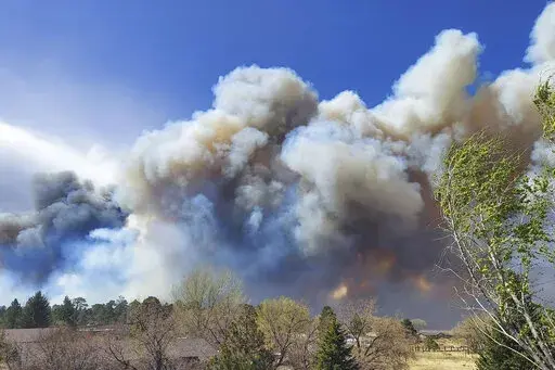 Smoke from a wind-whipped wildfire rises above neighborhoods on the outskirts of Flagstaff, Ariz., on Tuesday, April 19, 2022. Homes on the outskirts of Flagstaff were being evacuated Tuesday as high winds whipped a wildfire, shut down a major highway and grounded firefighting aircraft. (Sean Golightly/Arizona Daily Sun via AP)