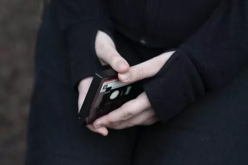A teenager holds her phone as she sits for a portrait near her home in Illinois, on Friday, March 24, 2023. The U.S. Surgeon General is warning there is not enough evidence to show that social media is safe for young people — and is calling on tech companies, parents and caregivers to take "immediate action to protect kids now." (AP Photo Erin Hooley, File)