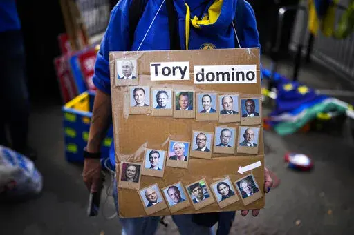 A protester holds a placard with photographs of British Prime Minister Boris Johnson, bottom right, his government cabinet members and Russia President Vladimir Putin, top left, outside the Houses of Parliament, in London, Wednesday, July 6, 2022. A defiant British Prime Minister Boris Johnson is battling to stay in power after his government was rocked by the resignation of two top ministers. His first challenge is getting through Wednesday, where he faces tough questions at the weekly Prime Mi