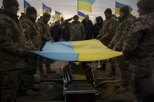 Ukrainian soldiers hold their national flag over the coffin of comrade Dmytro Kyrychenko, during his funeral in Bucha, outskirts of Kyiv, Ukraine, Friday, Dec. 23, 2022. The 33-year-old soldier died during a combat mission in the Donetsk region. (AP Photo/Felipe Dana)